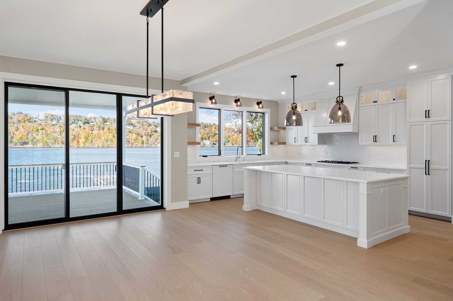 Bright white upper-level kitchen with a large island, glass sliders to a lake-view deck, and wide-plank oak floors - 148 North Lake Shore in Candlewood Shores on Candlewood Lake