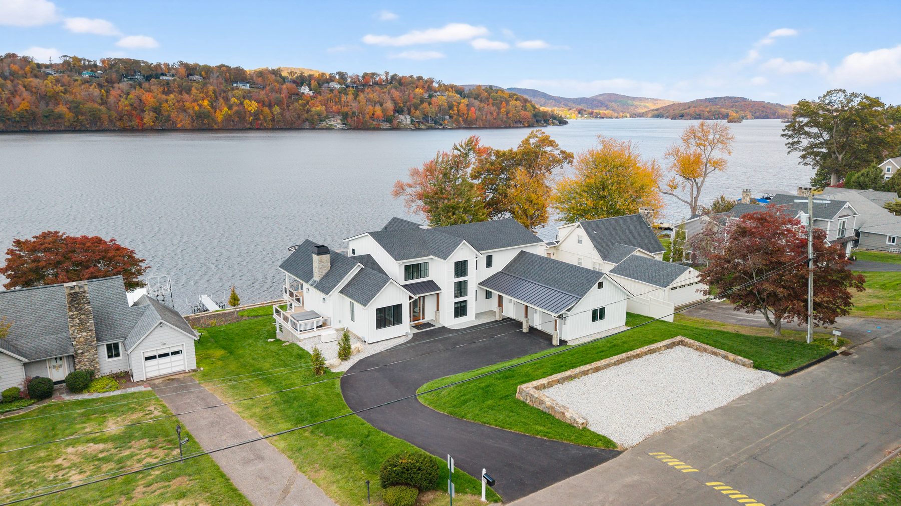 Aerial view of the custom home set on the shoreline amid autumn foliage with open water beyond - 148 North Lake Shore in Candlewood Shores on Candlewood Lake