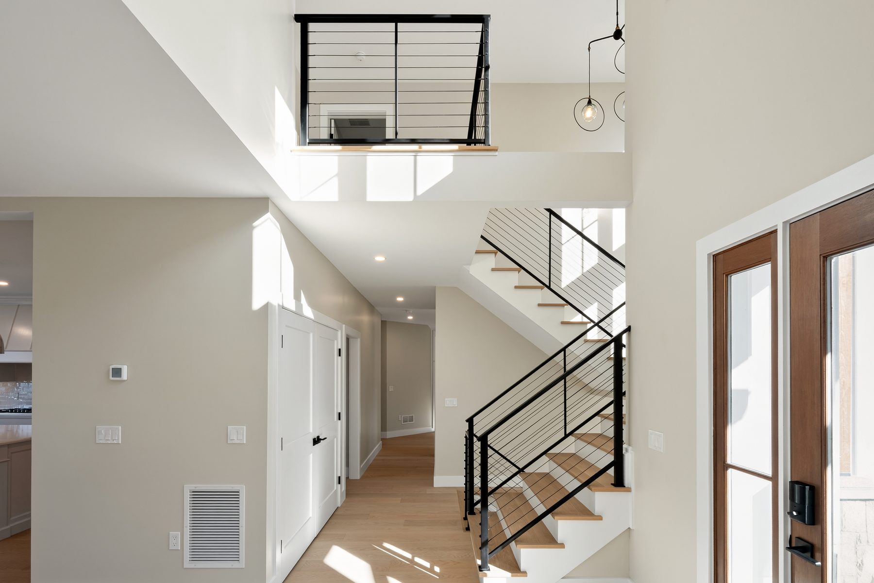 Two-story entry foyer with an open-riser oak staircase, black cable railings, and a wood-and-glass front door - 148 North Lake Shore, a custom lakefront home in Candlewood Shores on Candlewood Lake