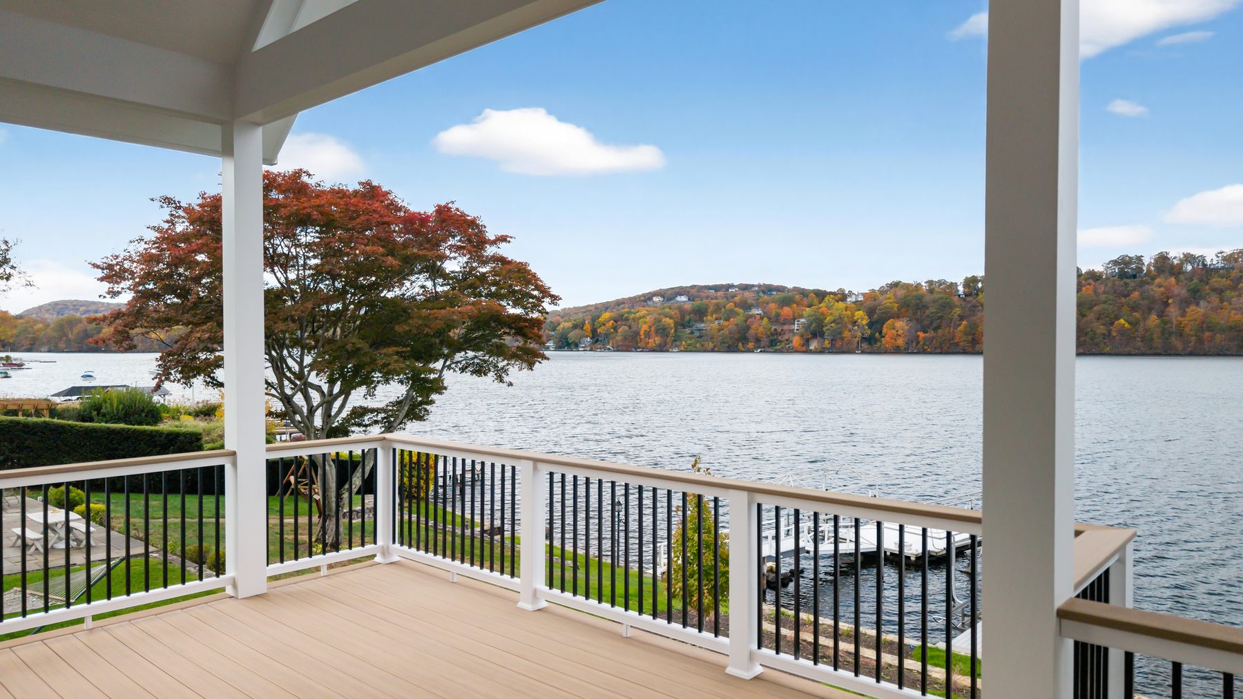 Covered porch framed by white columns overlooking Candlewood Lake, a private dock, and fall foliage - 148 North Lake Shore in Candlewood Shores