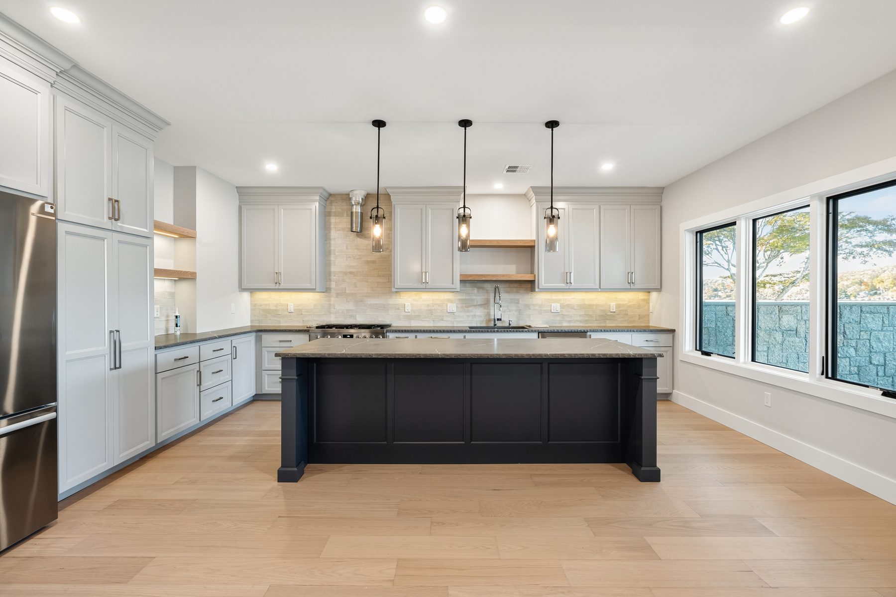 Lower-level great-room kitchen with a navy island, light-gray cabinetry, and a stone-tile backsplash - 148 North Lake Shore, a custom lakefront home in Candlewood Shores on Candlewood Lake