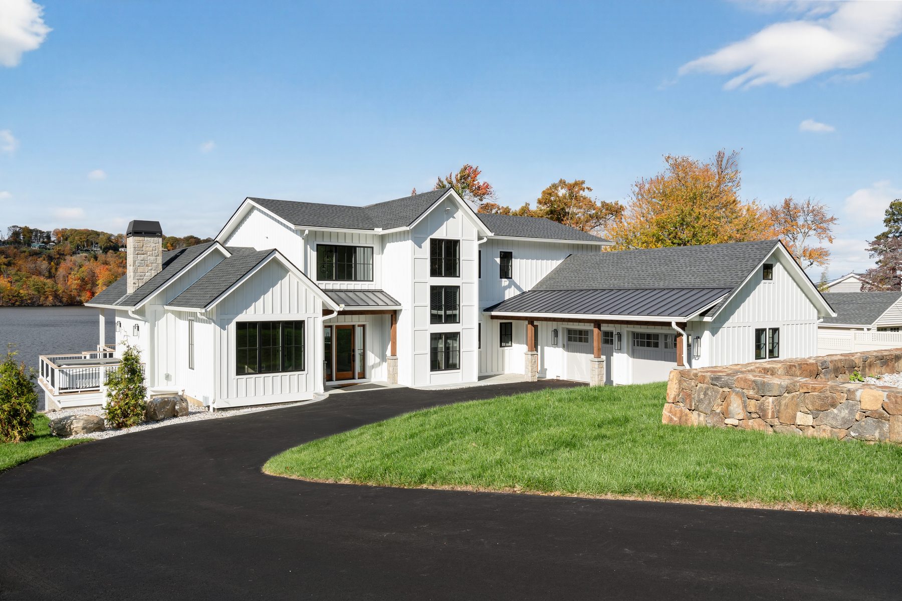 Ground-level front three-quarter view of the white farmhouse with stone chimney, curved drive, and stone retaining wall by the water - 148 North Lake Shore in Candlewood Shores on Candlewood Lake