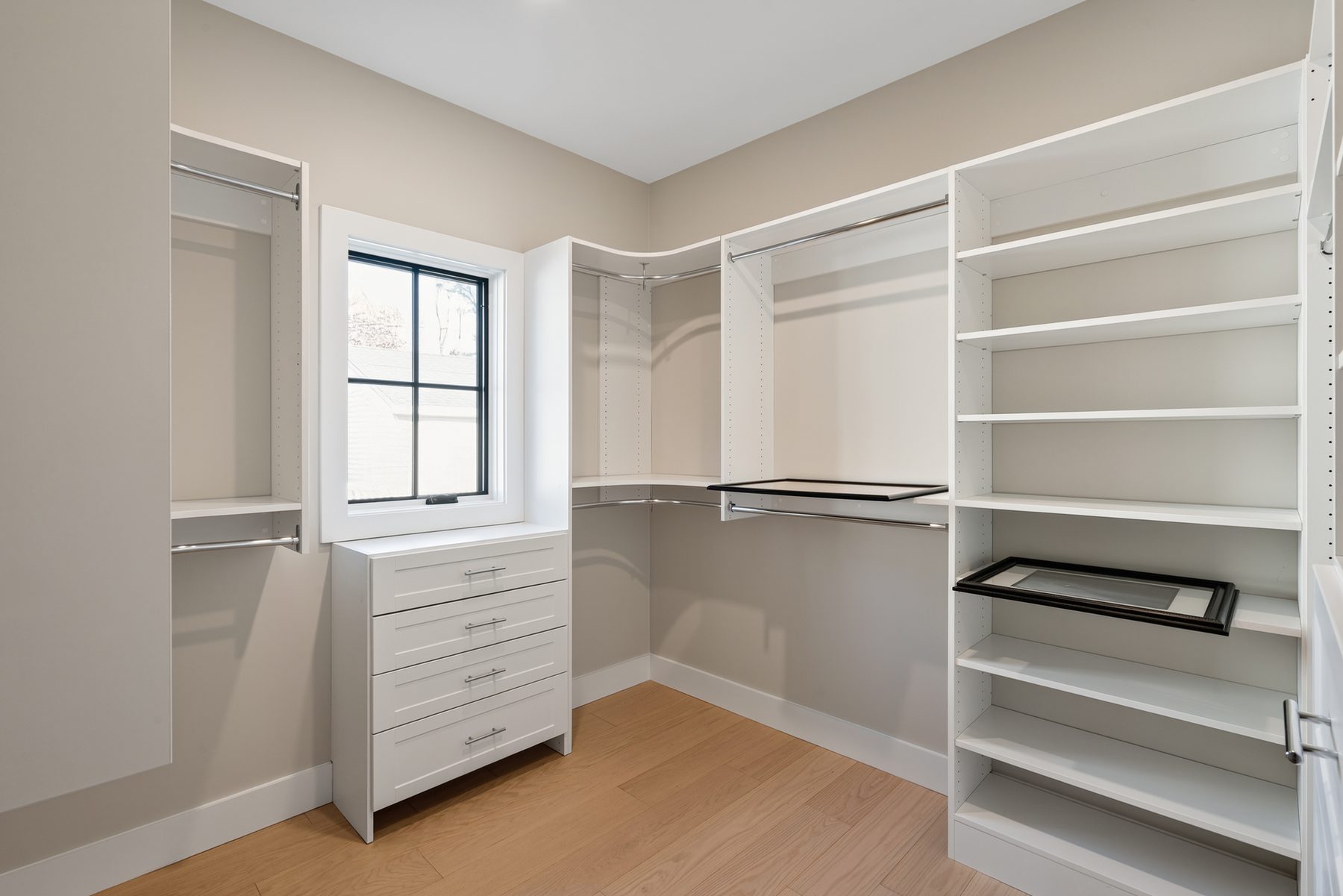 Walk-in closet outfitted with white built-in shelving, hanging rods, and a center dresser beneath a window - 148 North Lake Shore in Candlewood Shores on Candlewood Lake