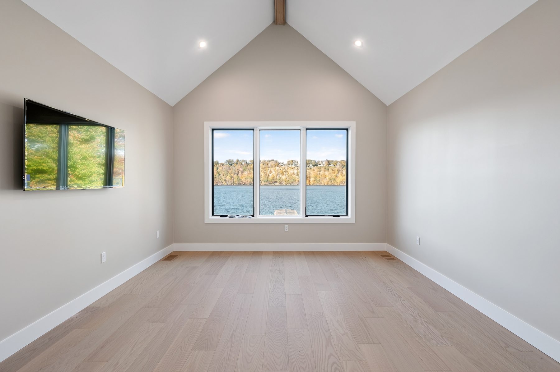 Vaulted bedroom with a paneled accent wall and a window framing treetop lake views - 148 North Lake Shore, a custom lakefront home in Candlewood Shores on Candlewood Lake