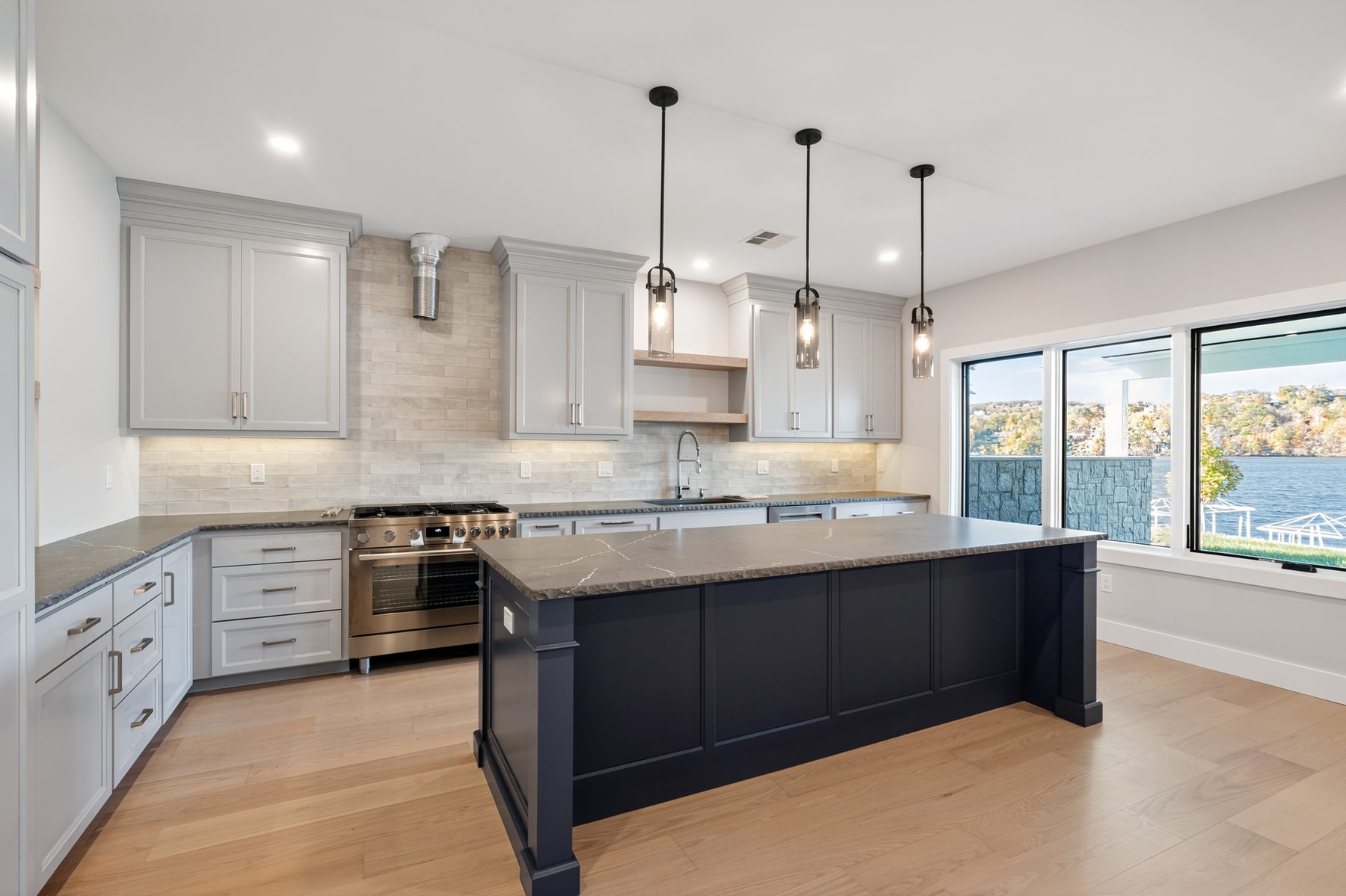Lower-level kitchen seen from the dining side, its navy island anchored beneath windows that open to the lake - 148 North Lake Shore in Candlewood Shores on Candlewood Lake