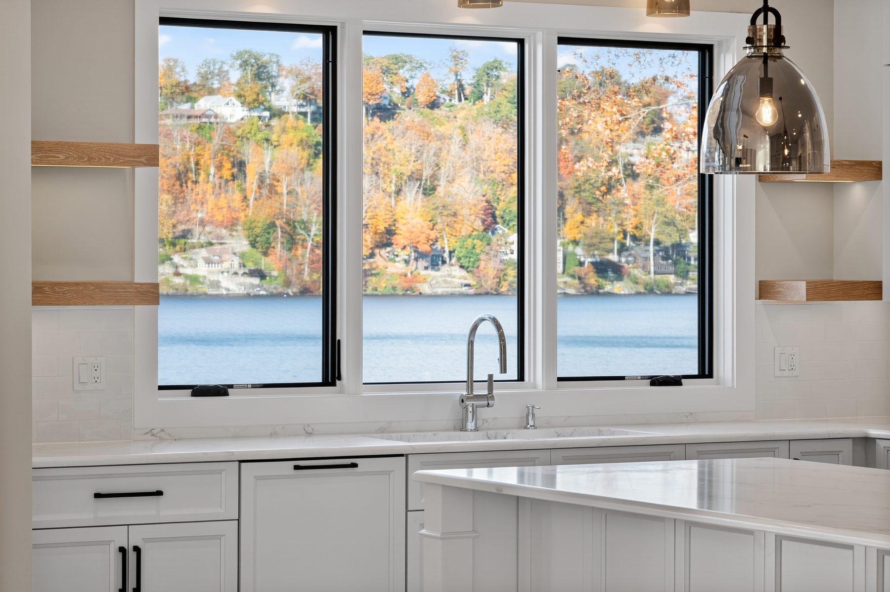 Detail of the white upper kitchen's range wall with a tile backsplash, floating shelves, and a sink window over the lake - 148 North Lake Shore in Candlewood Shores on Candlewood Lake