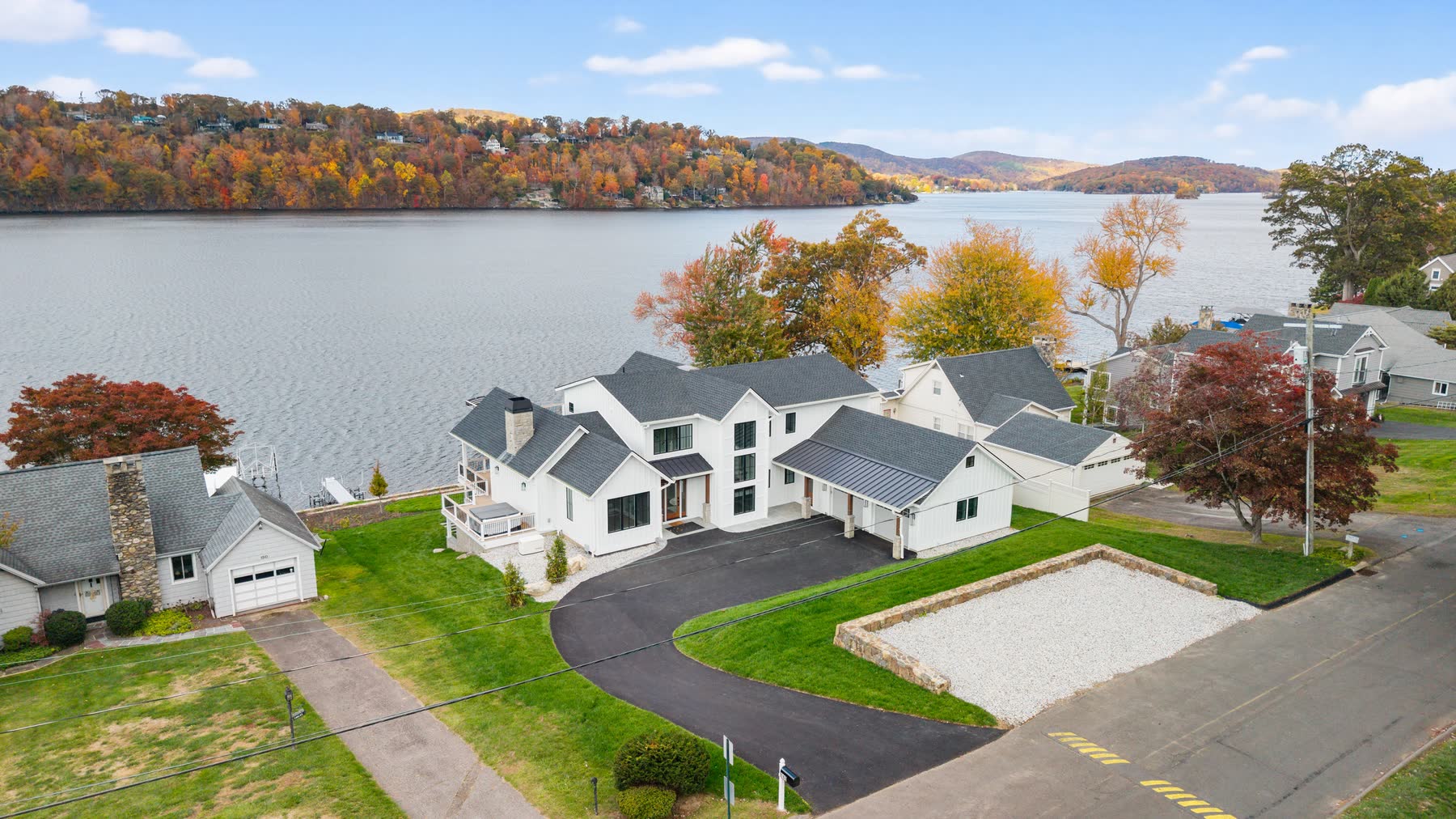 Aerial of the lakeside white farmhouse at 148 North Lake Shore, its drive and the autumn shoreline of Candlewood Lake beyond — Bulldog Enterprises.