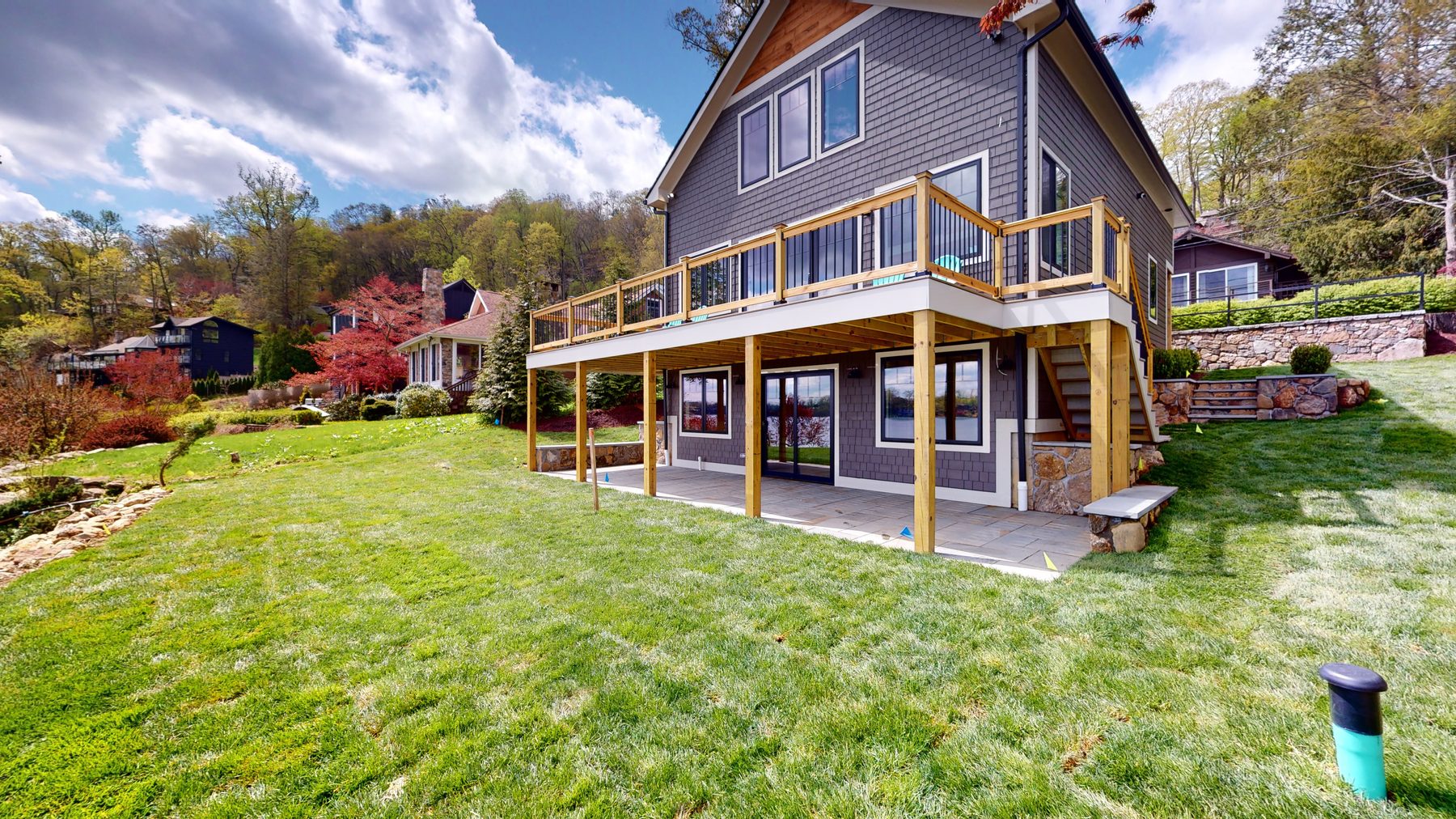 Rear facade of the gray shingled custom home with a two-tier deck above a covered bluestone patio and sweeping lawn — 3 Woods Road, a custom lakefront home in Candlewood Knolls on Candlewood Lake