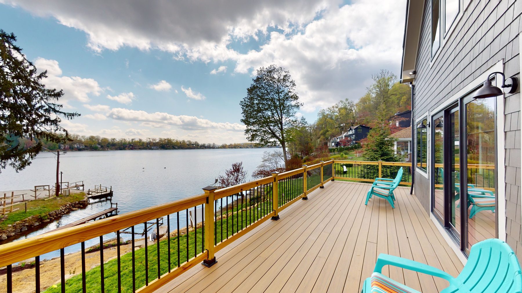 Lake-facing deck with wood railings and turquoise Adirondack chairs overlooking the water and dock — 3 Woods Road, a custom lakefront home in Candlewood Knolls on Candlewood Lake