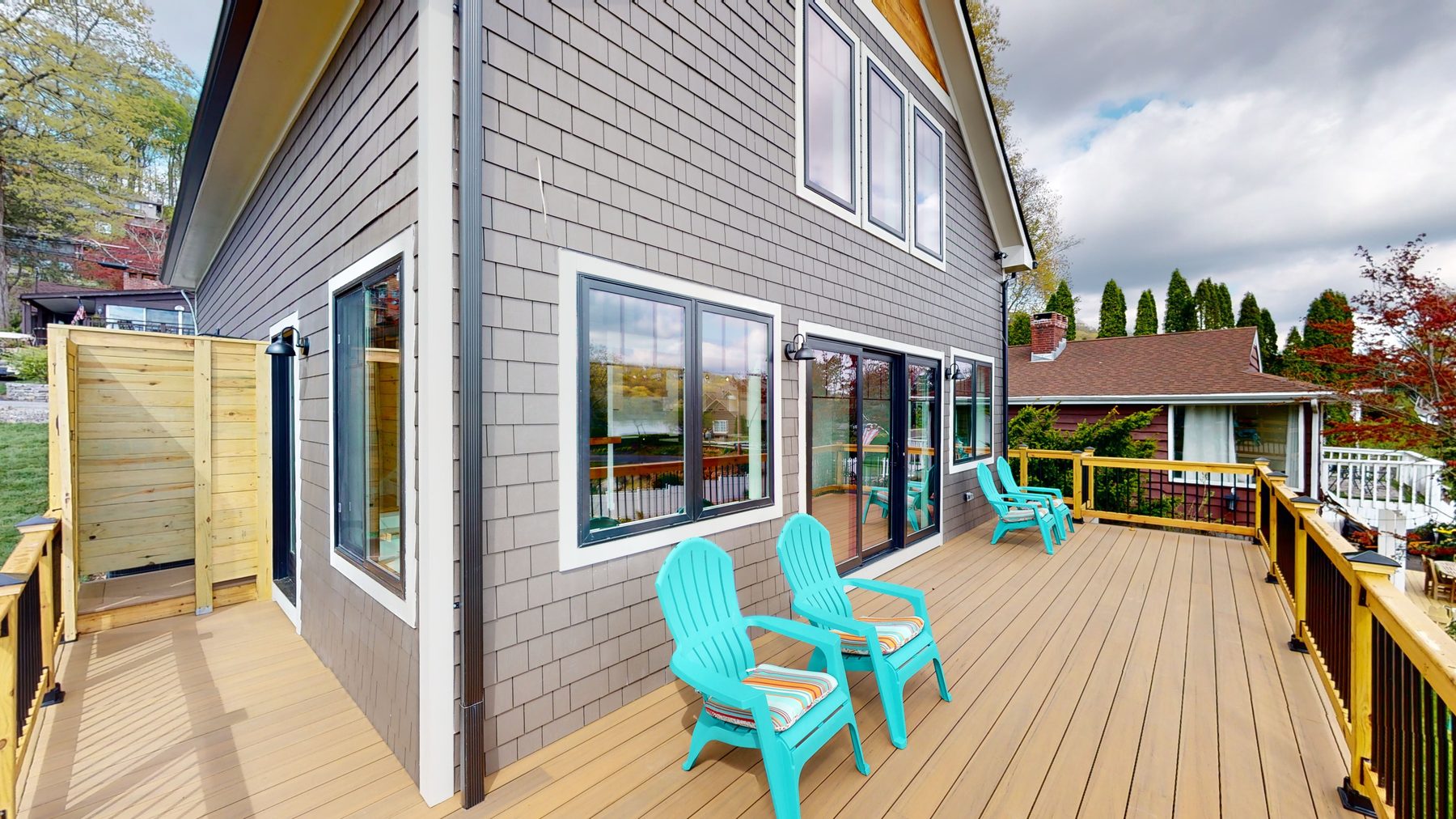 Wraparound deck with turquoise Adirondack chairs, an outdoor shower enclosure and gray shingle siding — 3 Woods Road, a custom lakefront home in Candlewood Knolls on Candlewood Lake