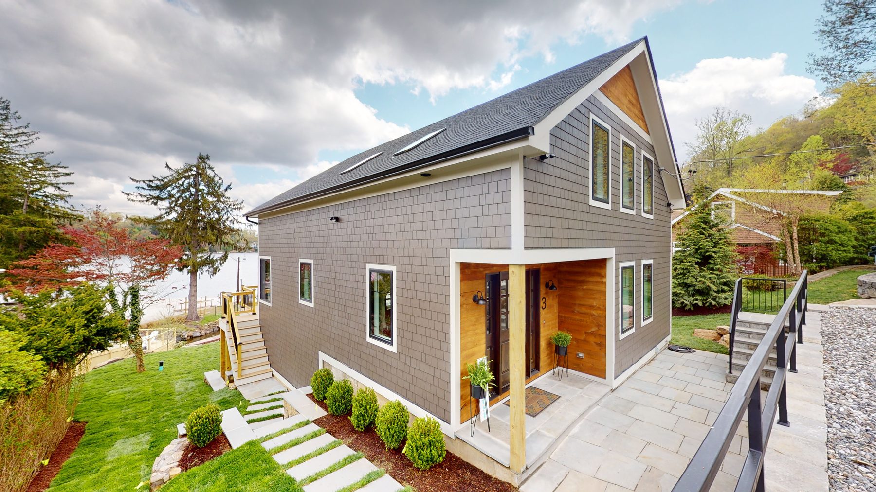 Three-quarter view of the gray shingled home showing the gabled roofline, skylights and bluestone walkway — 3 Woods Road, a custom lakefront home in Candlewood Knolls on Candlewood Lake