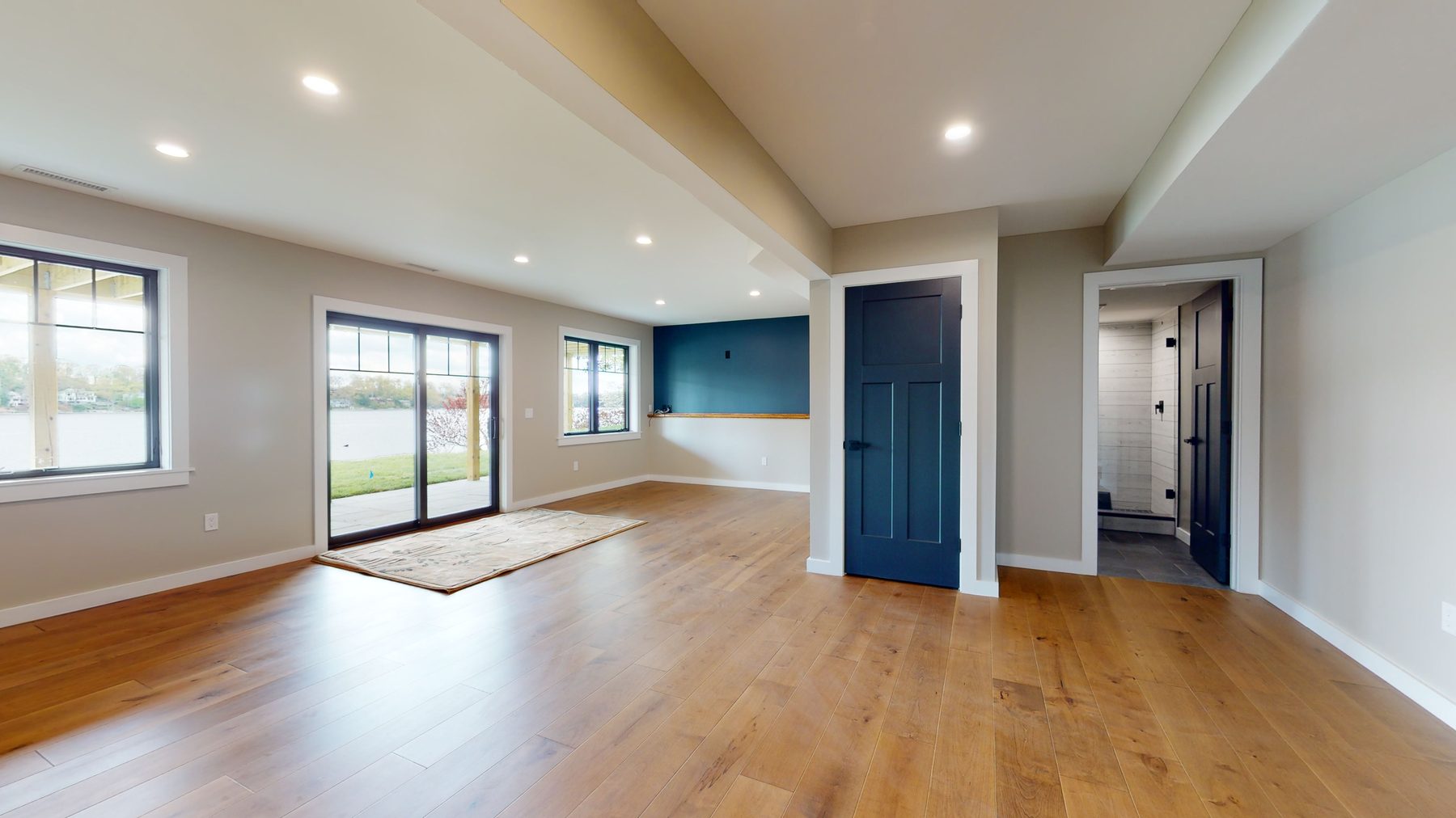 Lower-level family room in white oak flooring with sliding lake doors, a navy accent wall and an adjoining laundry — 3 Woods Road, a custom lakefront home in Candlewood Knolls on Candlewood Lake