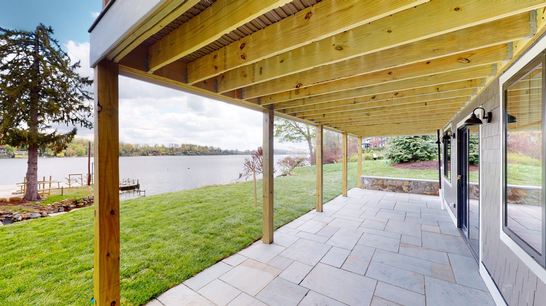 Covered bluestone patio beneath the deck with timber posts opening to the lawn and lake edge — 3 Woods Road, a custom lakefront home in Candlewood Knolls on Candlewood Lake