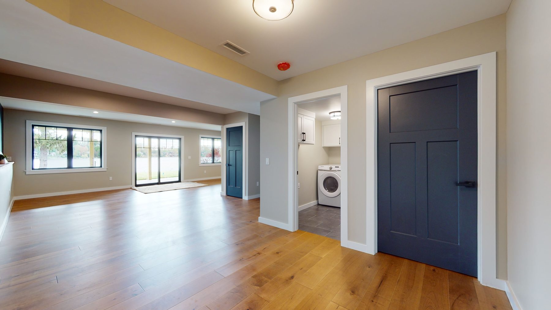 Lower-level living space in white oak flooring with lake-view sliders, navy doors and a quartz-topped wet bar — 3 Woods Road, a custom lakefront home in Candlewood Knolls on Candlewood Lake