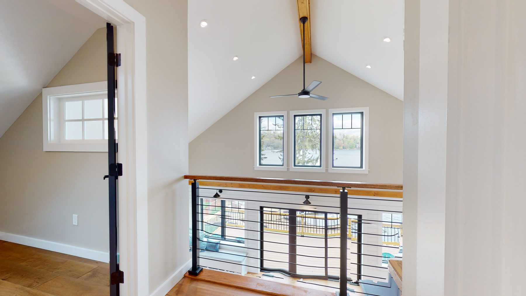 Loft landing with cable-and-wood railing overlooking the lake-view windows of the vaulted great room below — 3 Woods Road, a custom lakefront home in Candlewood Knolls on Candlewood Lake