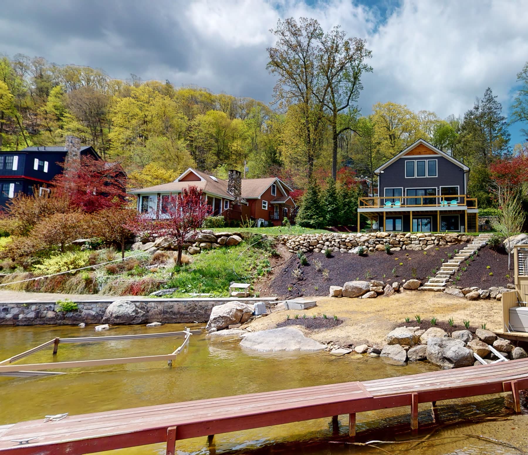 The custom lake home at 3 Woods Road seen from the water, set among neighboring cottages on the Candlewood Knolls shoreline — new construction by Bulldog Enterprises