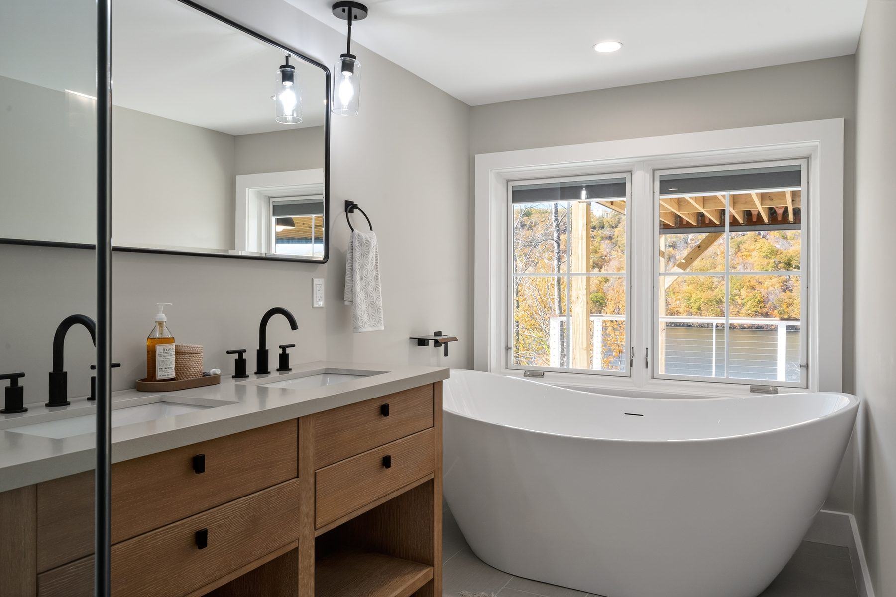 Primary bath with a freestanding soaking tub set at a corner window overlooking the lake and fall color - 43 Moody Lane, a custom home in Danbury, CT
