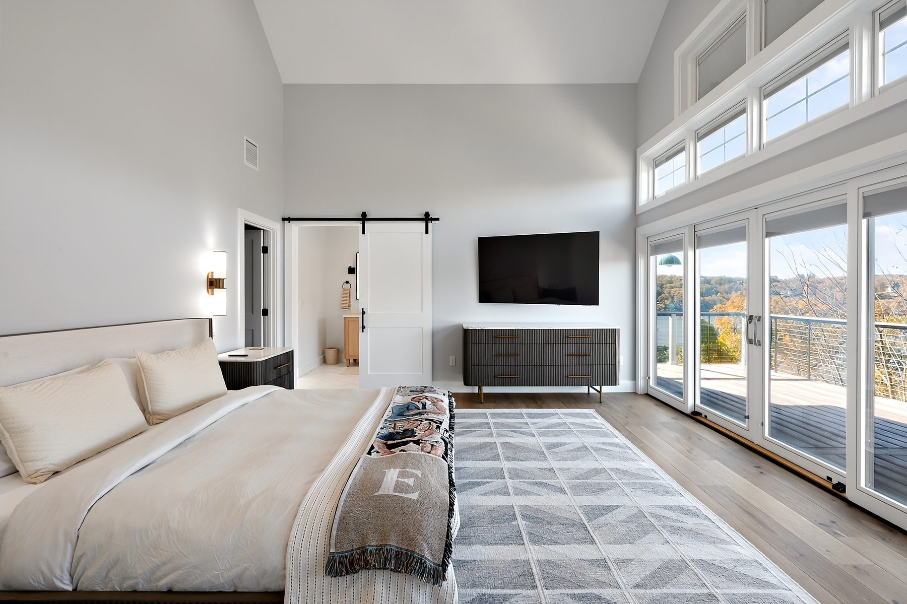 Vaulted primary bedroom with a wall of windows and sliding doors opening to a lake-view deck - 43 Moody Lane, a custom home in Danbury, CT