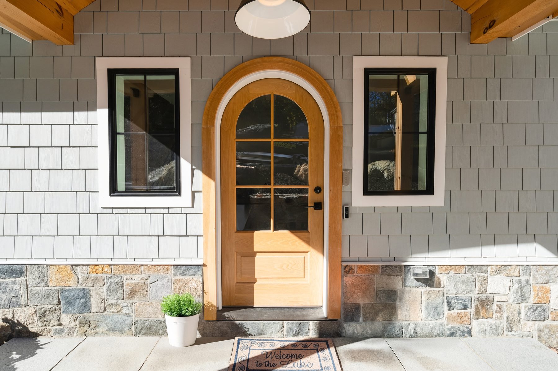Front entry detail with an arched natural-wood door framed by shingle siding and stone veneer - 43 Moody Lane, a custom home in Danbury, CT