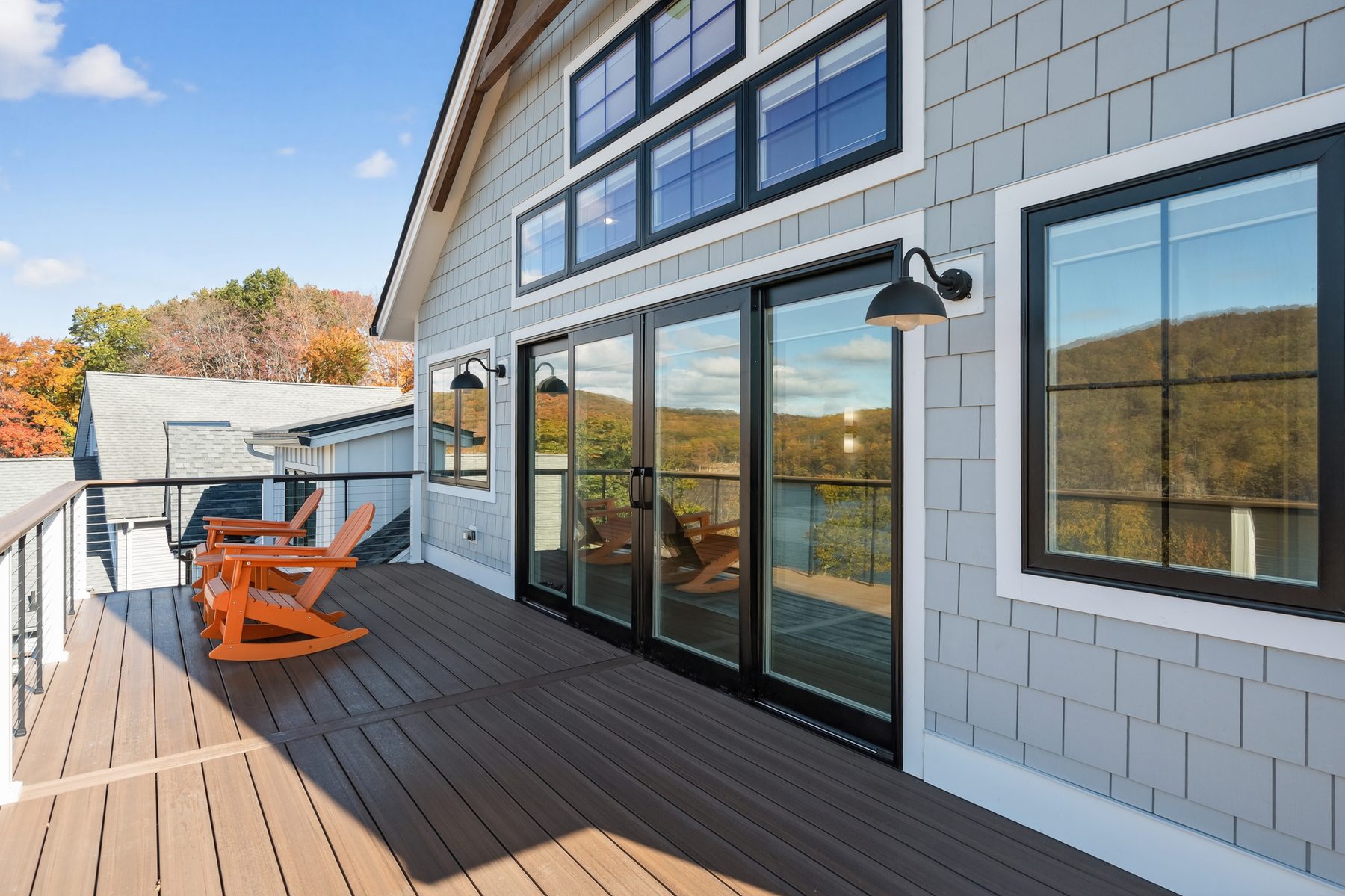 Covered deck with lounge chairs and black-framed windows looking out over the wooded lakeshore - 43 Moody Lane, a custom home in Danbury, CT