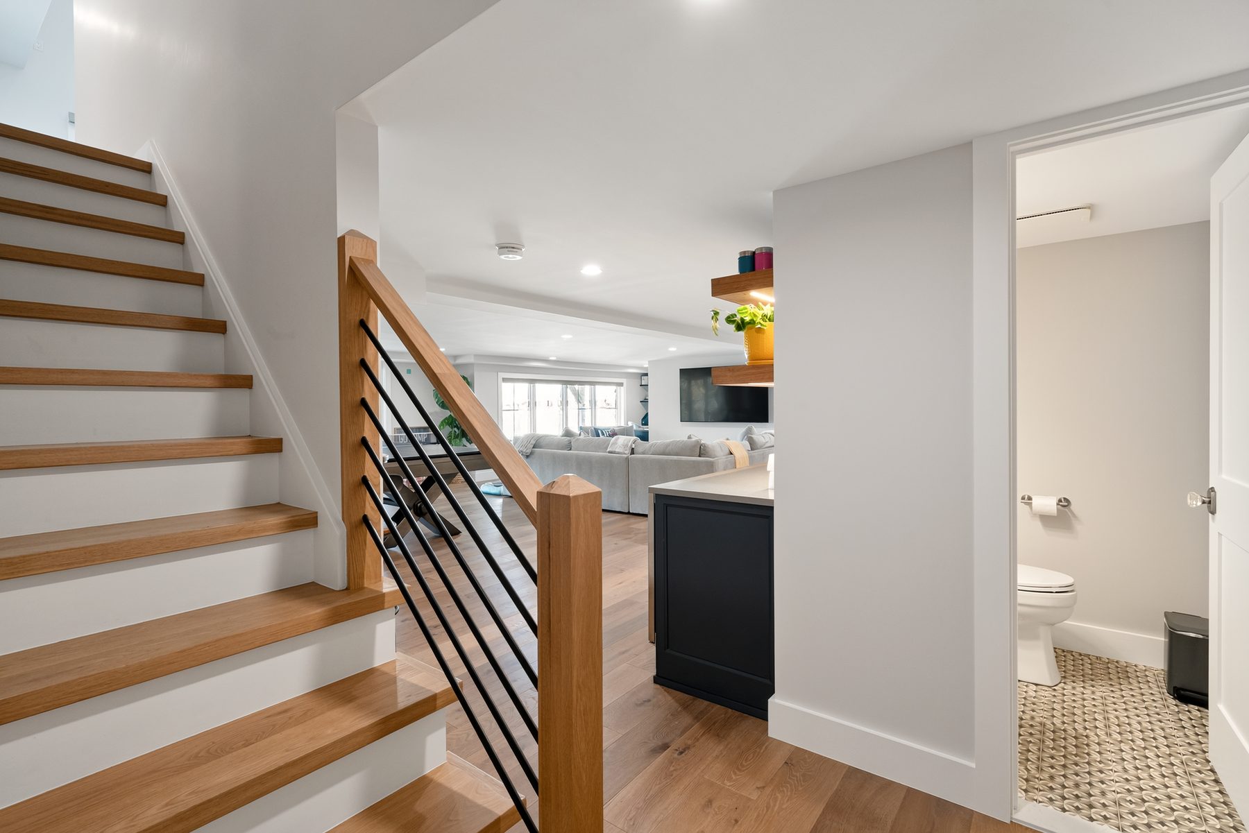 Open-tread oak staircase with a black metal railing beside a navy kitchen island and powder room - 43 Moody Lane, a custom home in Danbury, CT