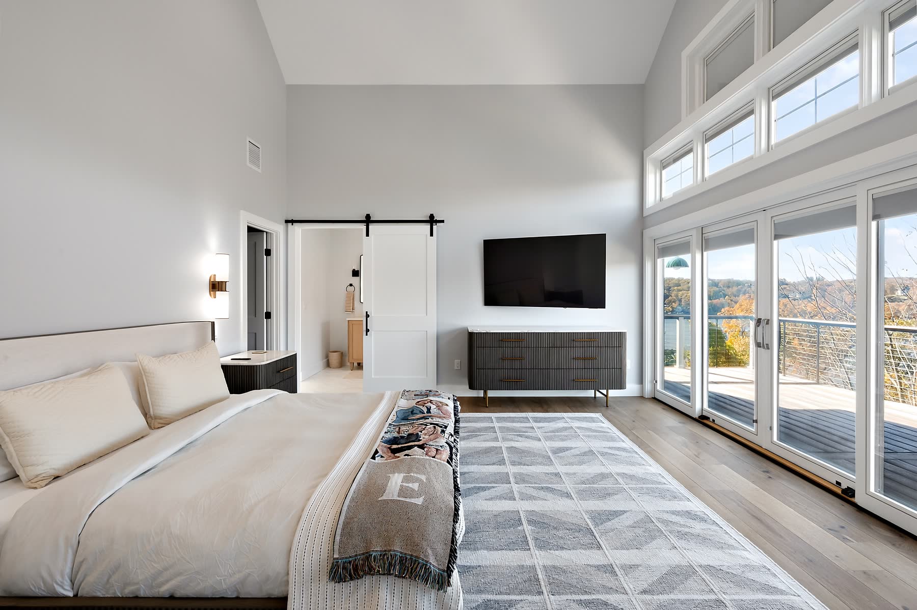 Vaulted primary bedroom at 43 Moody Lane with a barn-door bath entry and sliding glass doors opening to a lake-view deck — Bulldog Enterprises.
