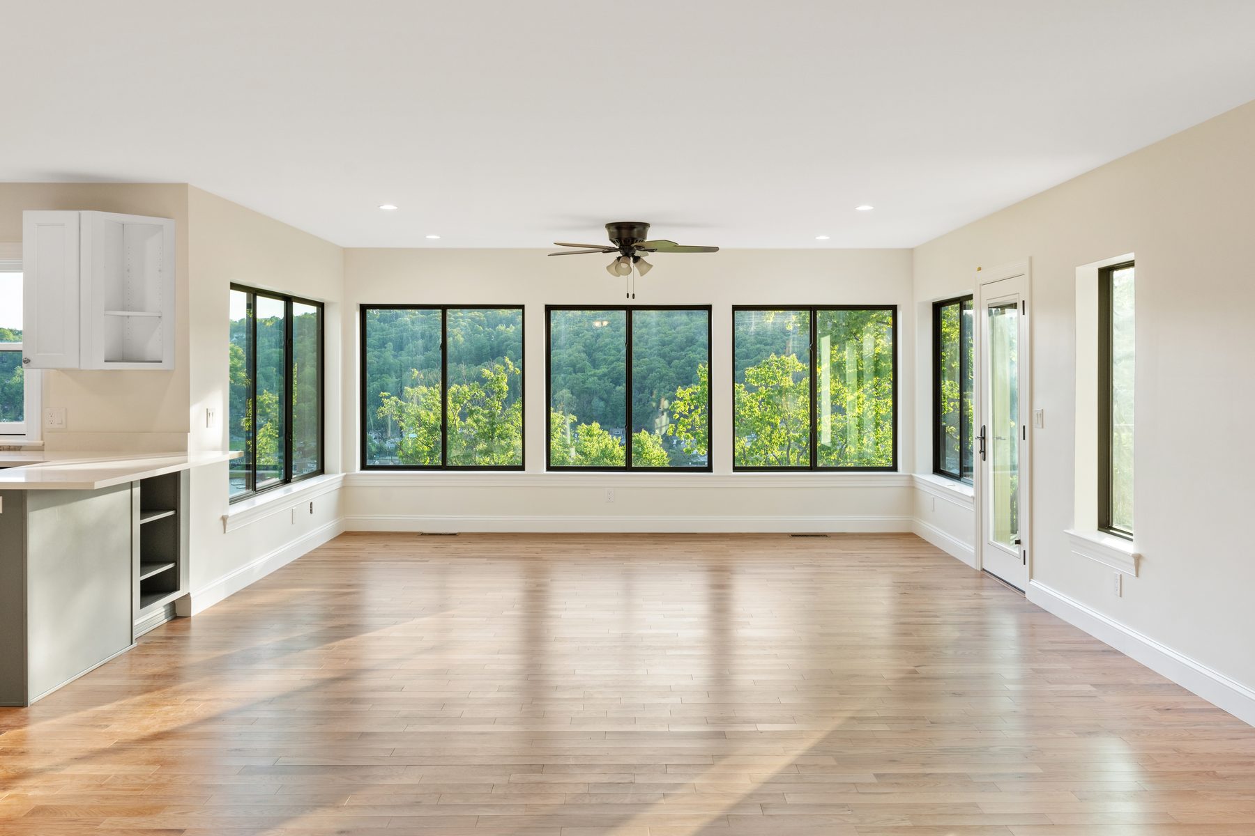 Sun-filled living room wrapped in a bank of black-framed windows over treetop lake views - 48 Ridge Road, a renovated lake home on Candlewood Isle