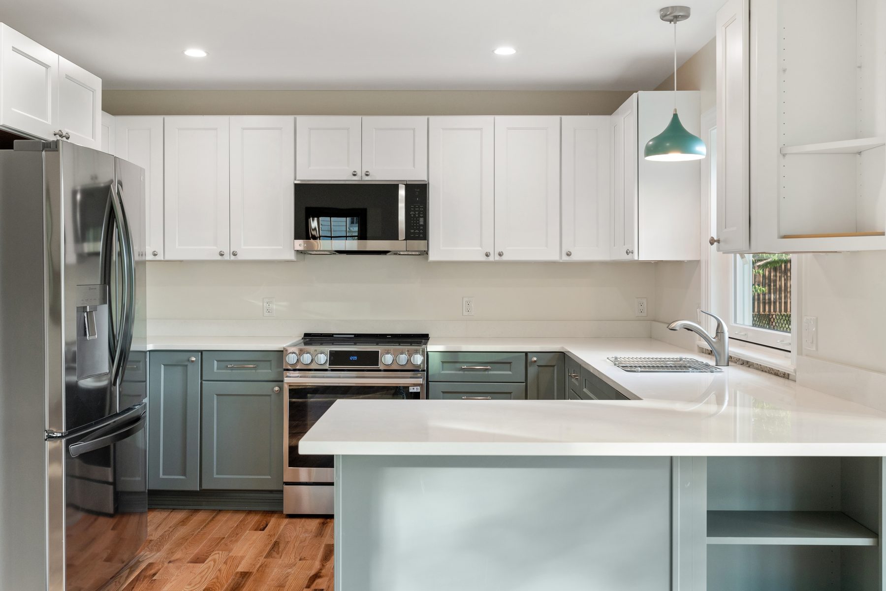 Renovated kitchen pairing white uppers with sage-green base cabinets, quartz counters and a teal pendant peninsula - 48 Ridge Road on Candlewood Isle