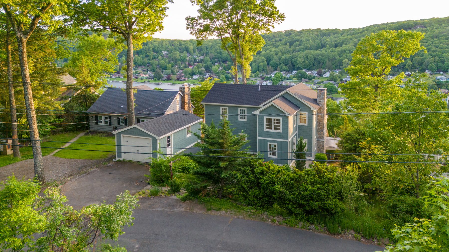 Aerial side view at dusk capturing the home, attached garage and driveway against the wooded Candlewood Lake hillside - 48 Ridge Road on Candlewood Isle