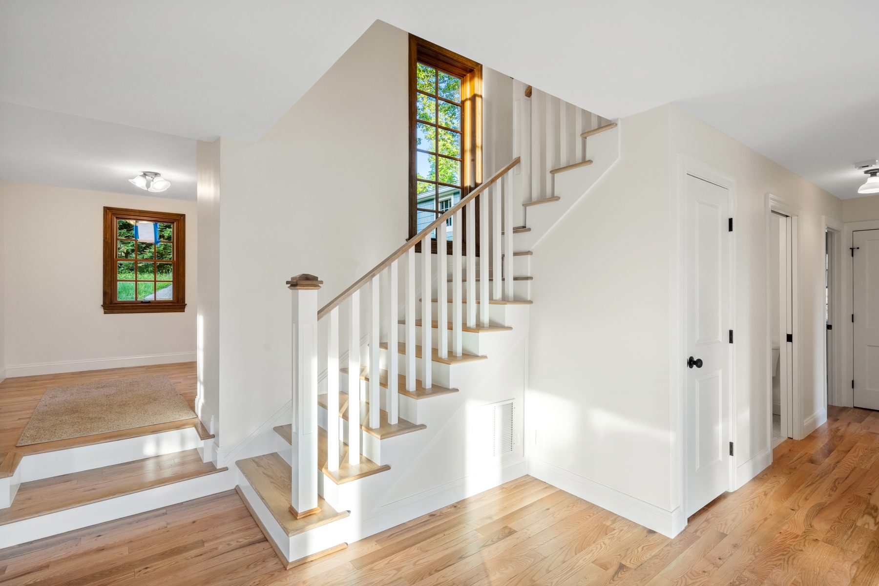 Bright entry foyer with a white open-baluster staircase and stained-wood landing window - 48 Ridge Road, a renovated lake home on Candlewood Isle