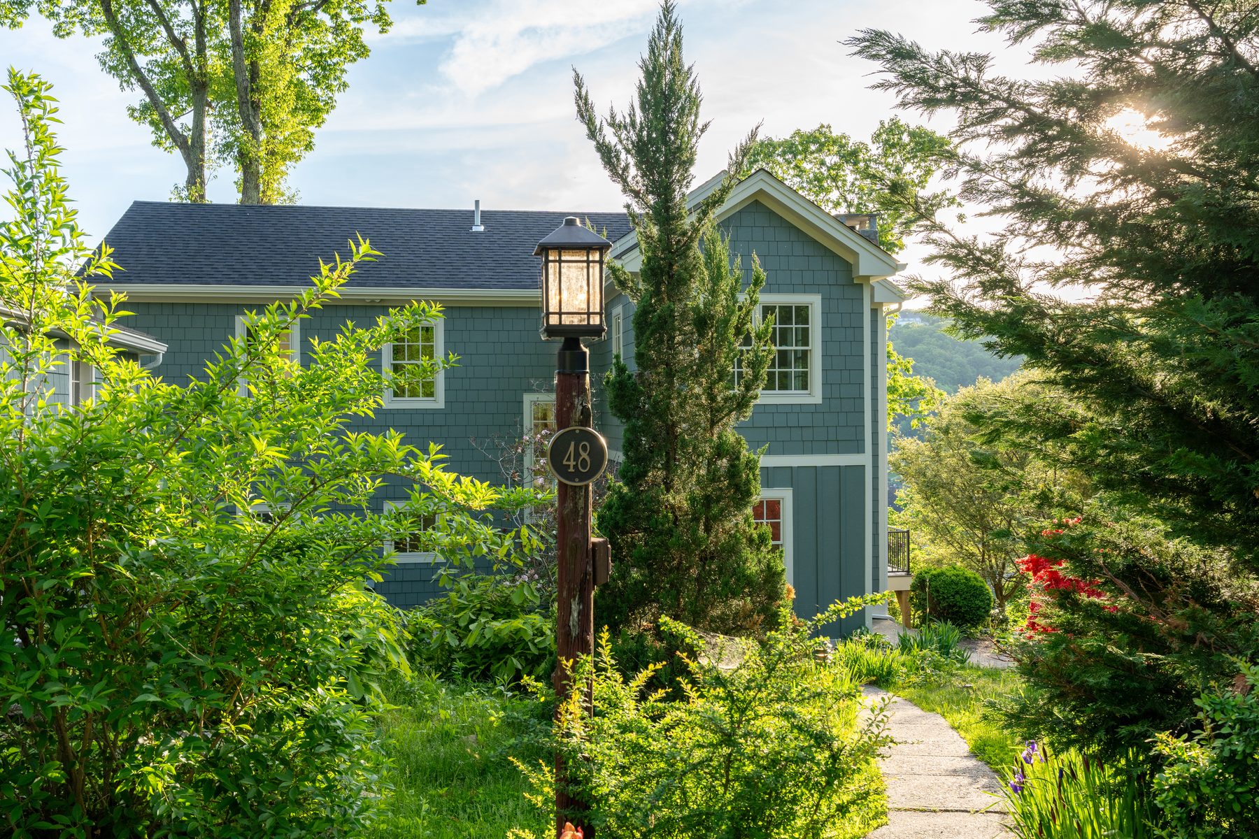 Sunlit front facade of the gabled second-floor addition with a flowering red azalea in the foreground - 48 Ridge Road on Candlewood Isle