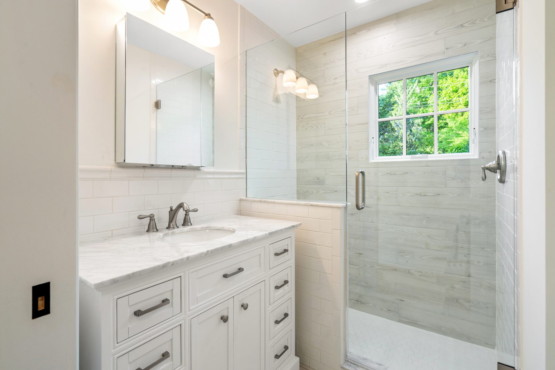 Guest bath with white shaker vanity, marble top and a wood-look tiled glass shower beside a garden window - 48 Ridge Road on Candlewood Isle