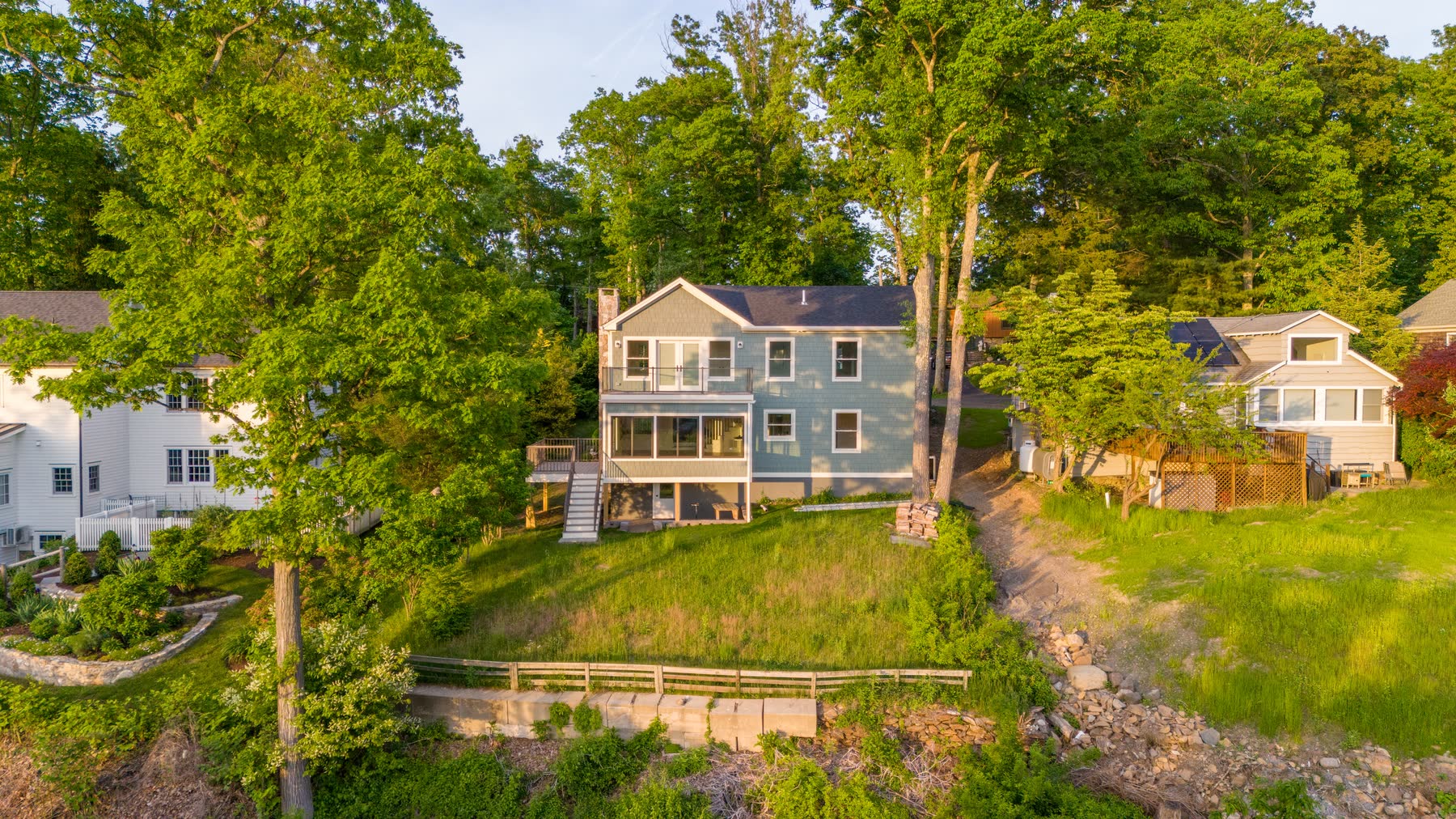 Golden-hour aerial of the renovated cedar-shingle home at 48 Ridge Road, set into the wooded hillside above Candlewood Lake — Bulldog Enterprises.