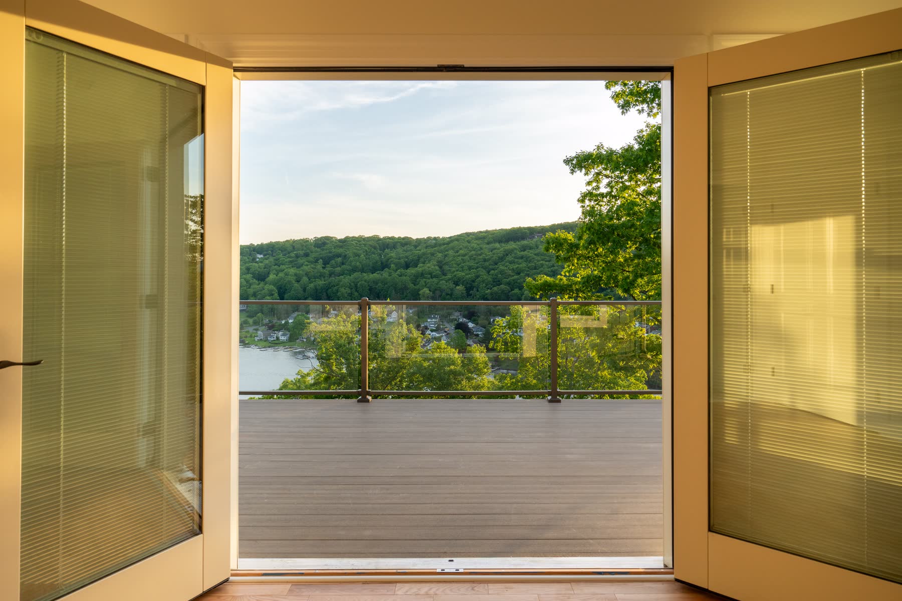 Sliding doors at 48 Ridge Road opening onto a cantilevered deck with a glass railing and a sweeping view across Candlewood Lake to the hills — Bulldog Enterprises.