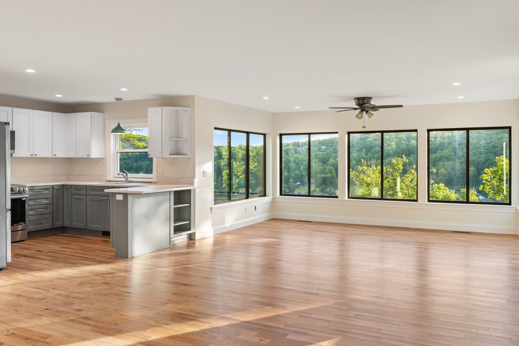 Open great room and white kitchen at 48 Ridge Road wrapped in black-framed windows over the lake, with white-oak floors — renovation by Bulldog Enterprises.