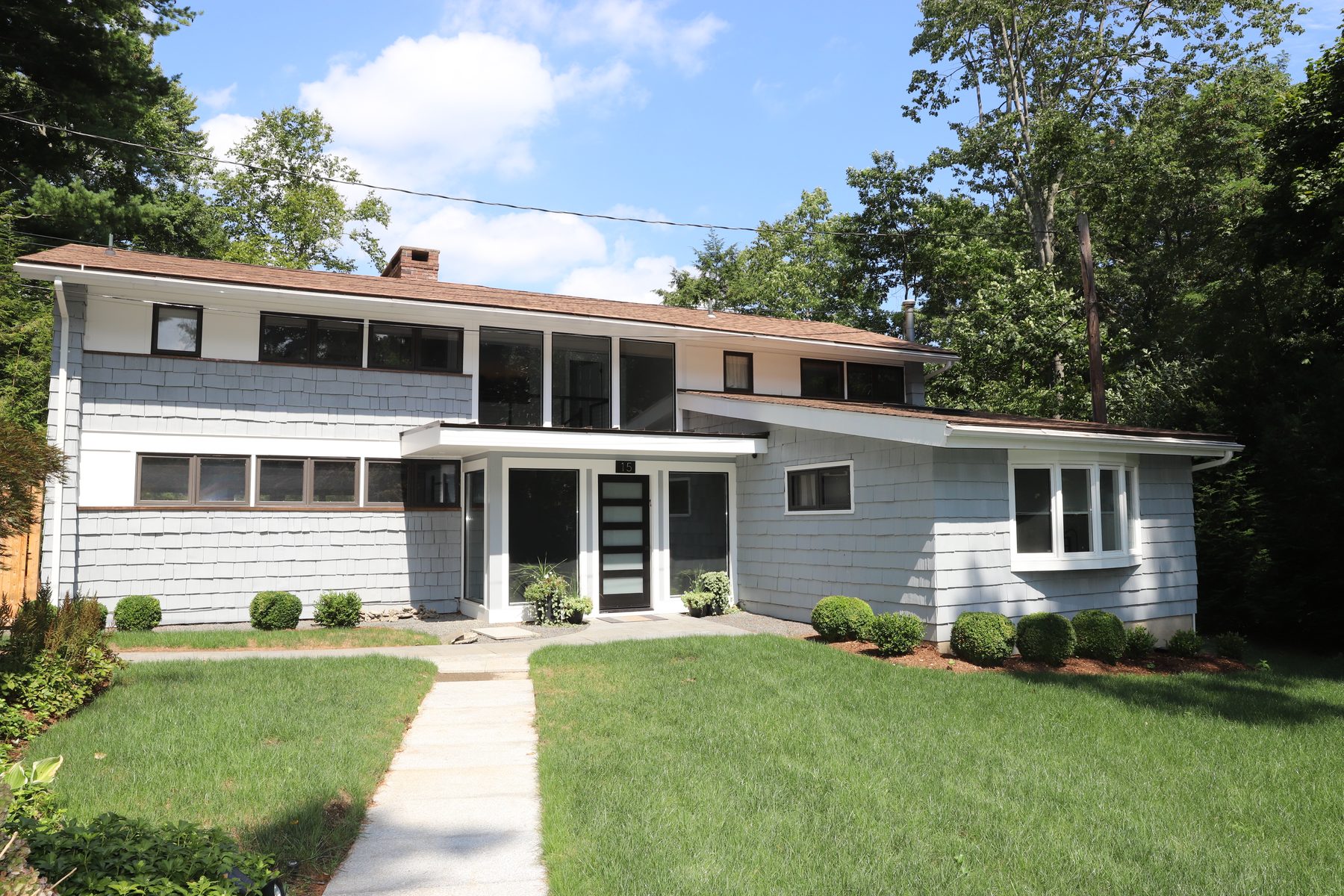 Front facade of the mid-century-modern home with cedar-shingle siding, ribbon windows and a stone walkway across the lawn - Sunset Drive, a renovated lake home on Candlewood Lake