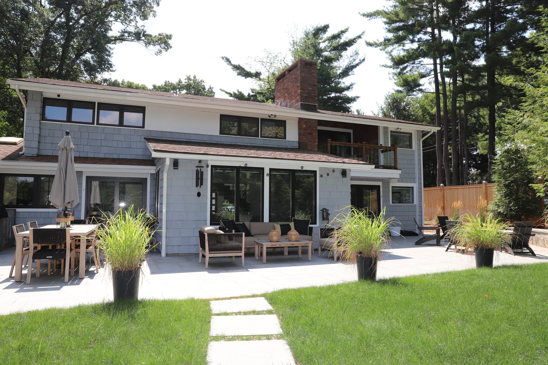Lakeside rear elevation with shingle siding and brick chimney over a bluestone patio set with a sectional and dining table - Sunset Drive, a renovated lake home on Candlewood Lake