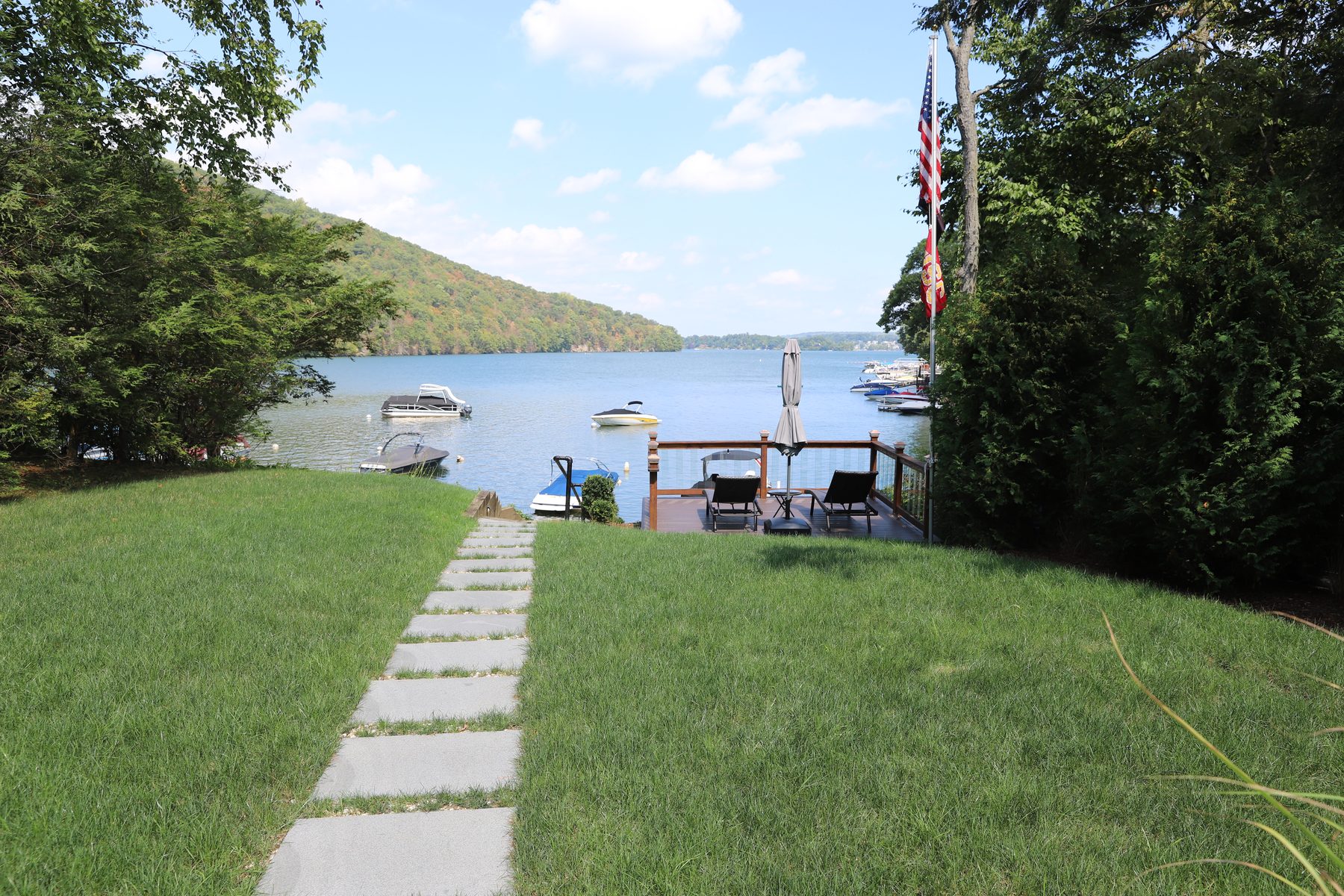 Lakefront lawn with a stone-slab path leading down to a private dock and boats moored on Candlewood Lake - Sunset Drive, a renovated lake home in Connecticut