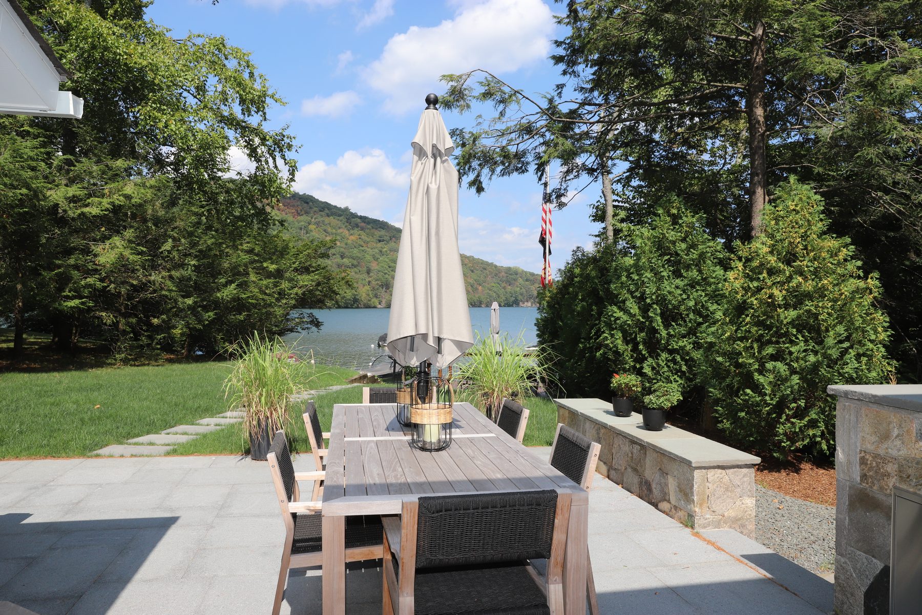 Bluestone patio dining area with an umbrella-shaded teak table and a low stone seat wall framing the lake view - Sunset Drive, a renovated lake home on Candlewood Lake