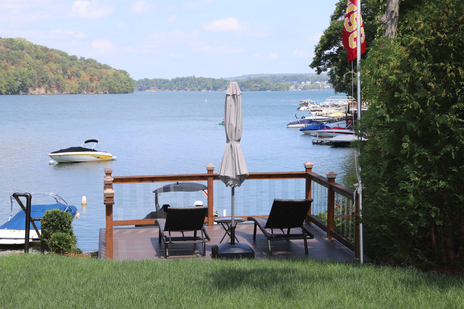 Lakefront deck with lounge chairs and an umbrella overlooking boats on the water at Candlewood Lake - Sunset Drive, a renovated lake home in Connecticut