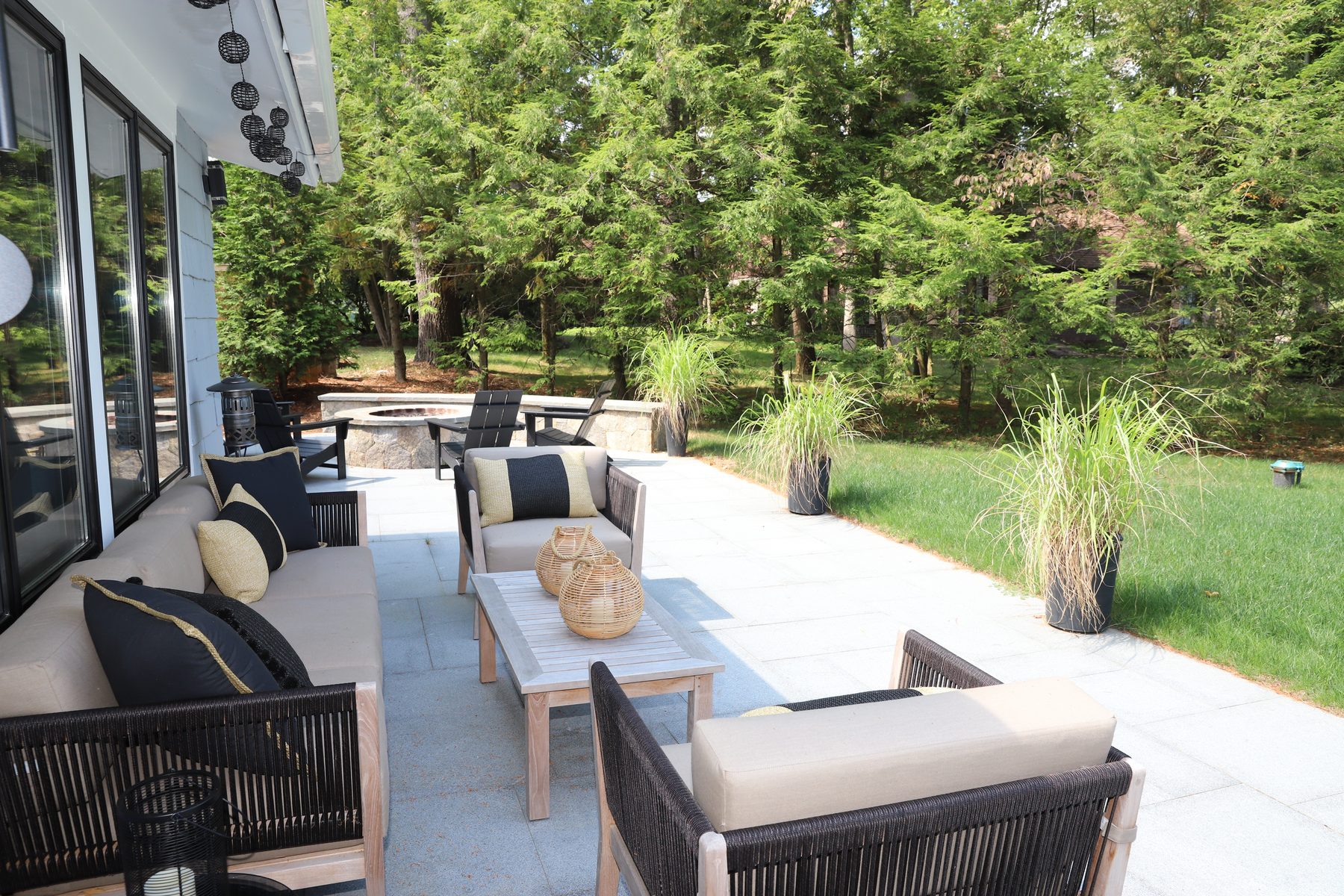 Patio lounge with cushioned outdoor seating and a fire pit set against a backdrop of tall evergreens - Sunset Drive, a renovated lake home on Candlewood Lake