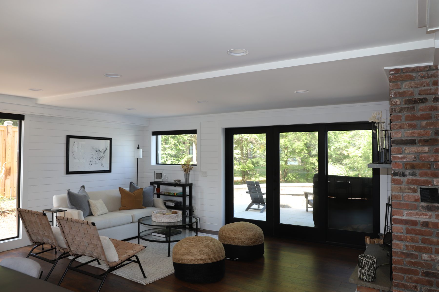Sun-filled living room with black-framed sliding glass doors opening to the deck beside a brick chimney column - Sunset Drive, a renovated lake home on Candlewood Lake