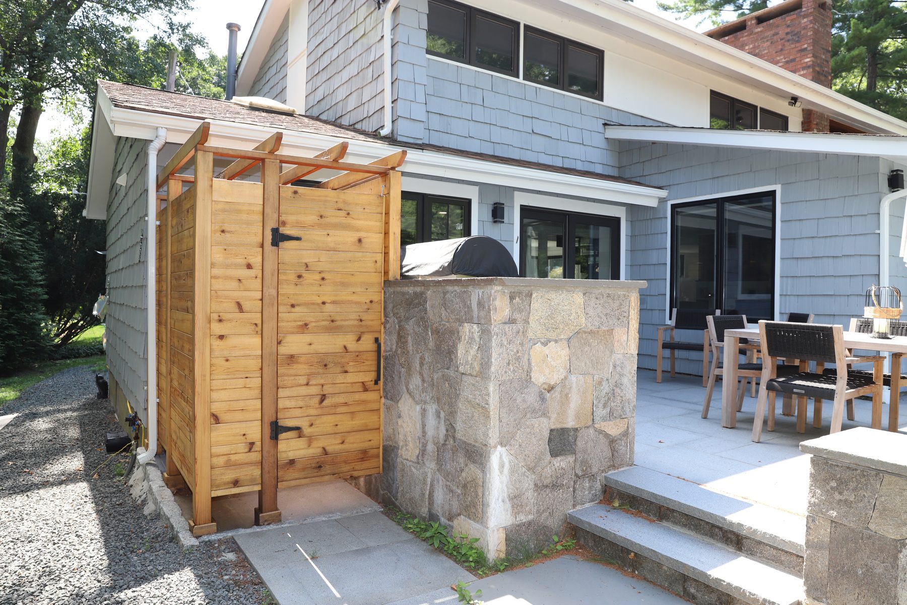 Cedar-clad outdoor shower enclosure next to the stone outdoor-kitchen base on the side patio - Sunset Drive, a renovated lake home on Candlewood Lake