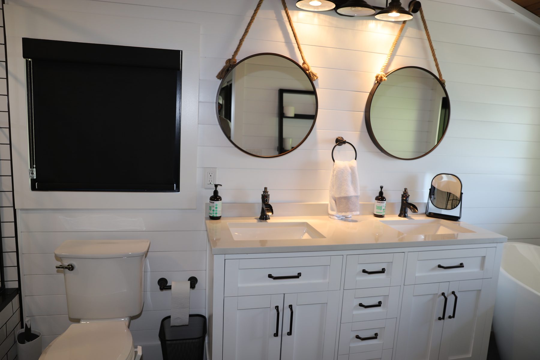 Double-vanity bath with twin rope-hung round mirrors, white shaker cabinetry and shiplap walls - Sunset Drive, a renovated lake home on Candlewood Lake