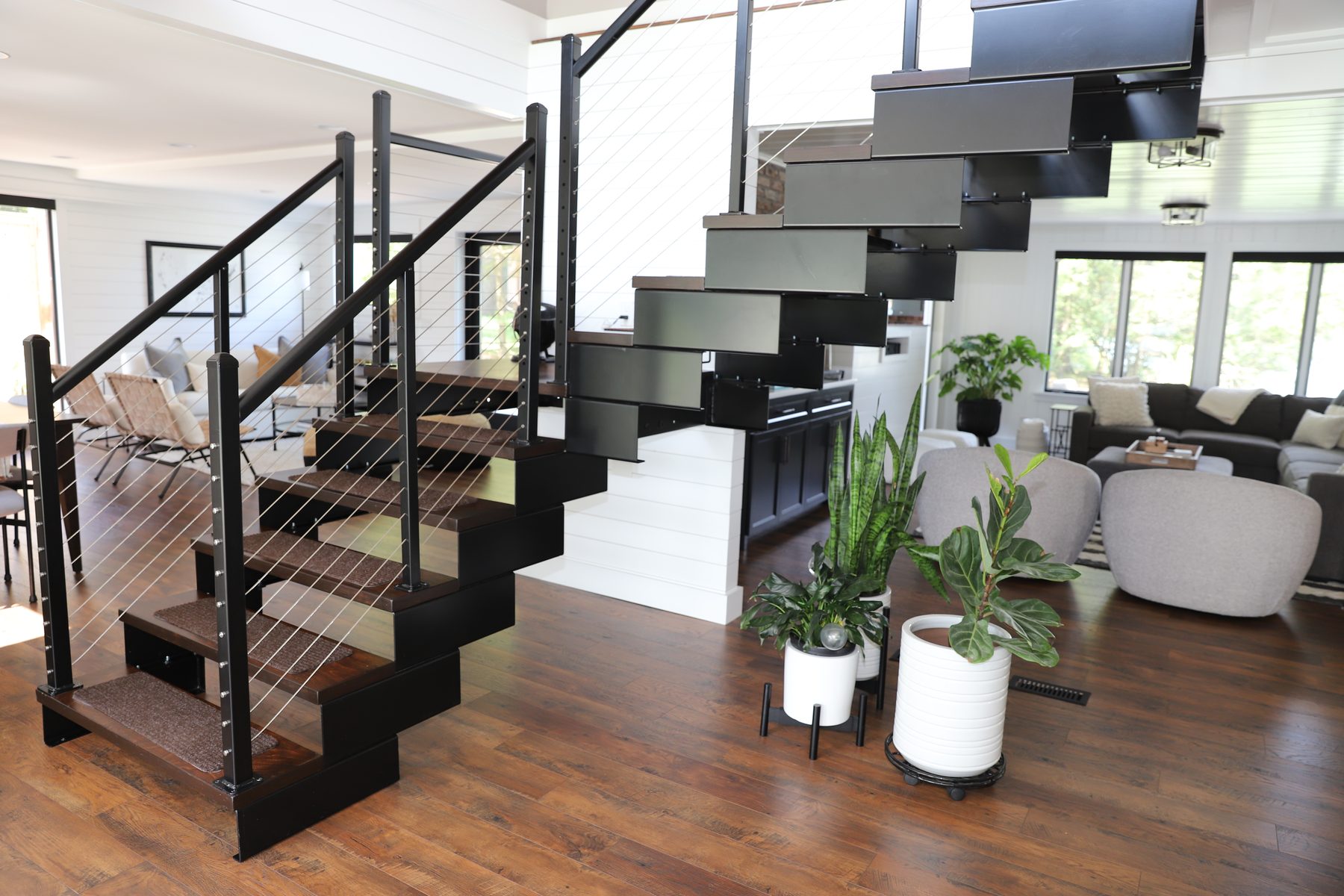 Floating steel staircase with cable railing rising through the open living area over warm hardwood floors - Sunset Drive, a renovated lake home on Candlewood Lake