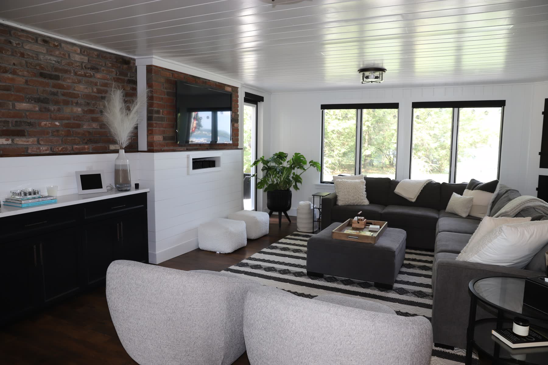 Living room at Sunset Drive with an exposed-brick accent wall, white shiplap, a beadboard ceiling and a sectional by the windows — Bulldog Enterprises.
